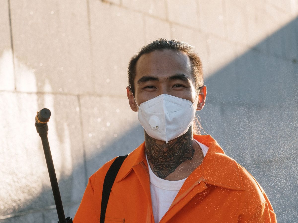 Pest control technician in a mask holding a sprayer wand
